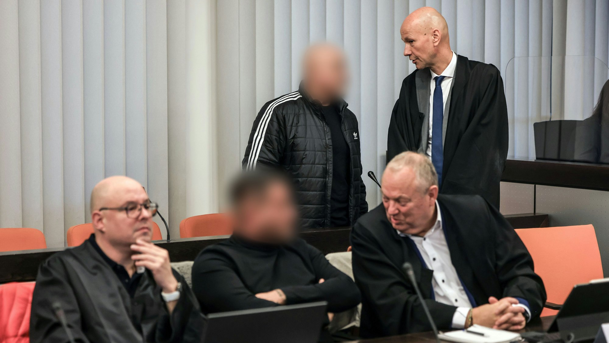 Der Hauptangeklagte (hinten, links) spricht im Gerichtssaal mit seinem Verteidiger Oliver Doelfs (hinten, rechts), während vorne ein Angeklagter (M) mit seinem Verteidiger Hartmut Moyzio (vorne, rechts) spricht.