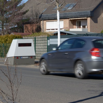 Ein Auto nähert sich einer Geschwindigkeitsmessanlage, die am Straßenrand steht.