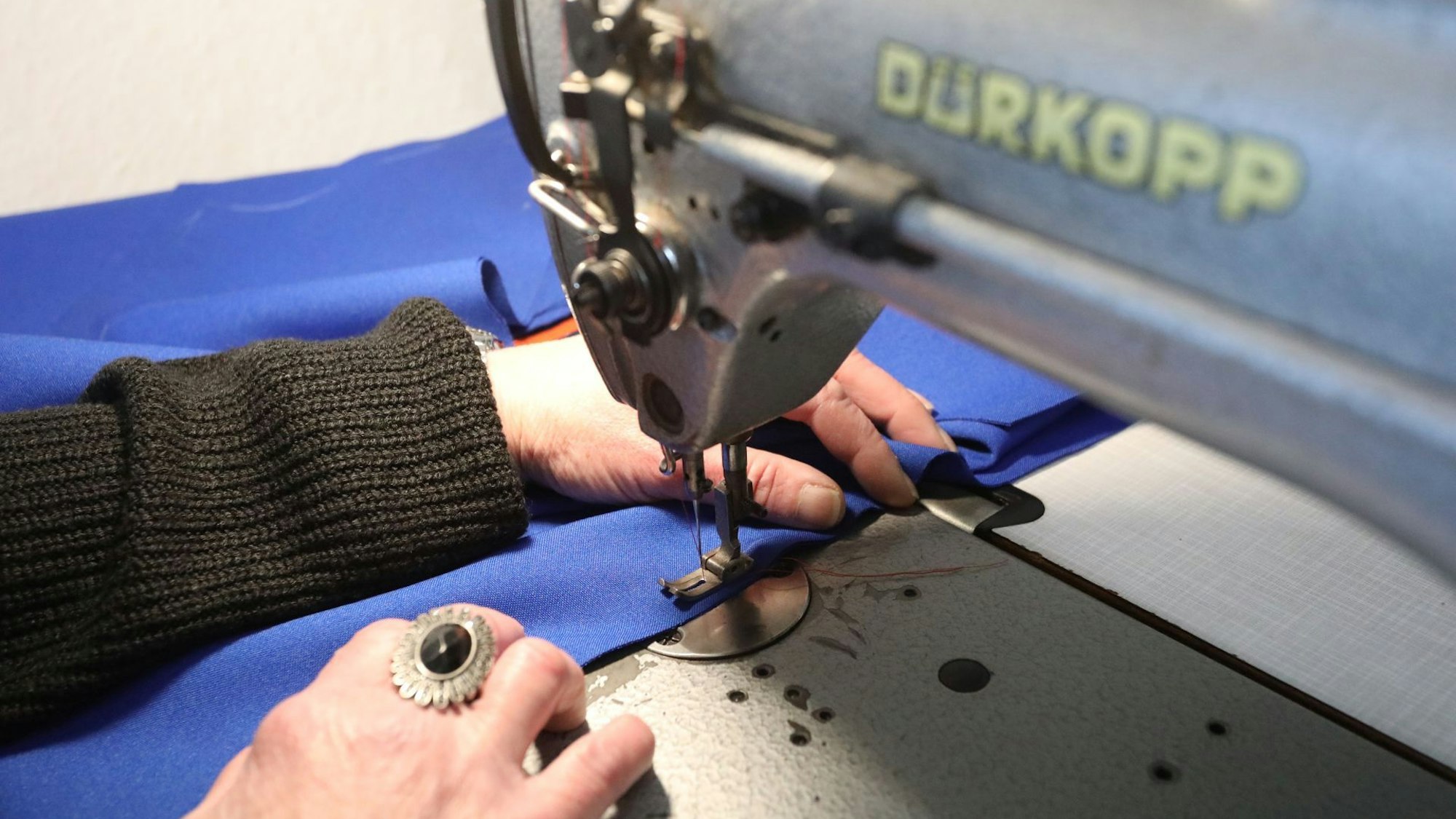 An einer Nähmaschine wird an einem blauen Stoff genäht.