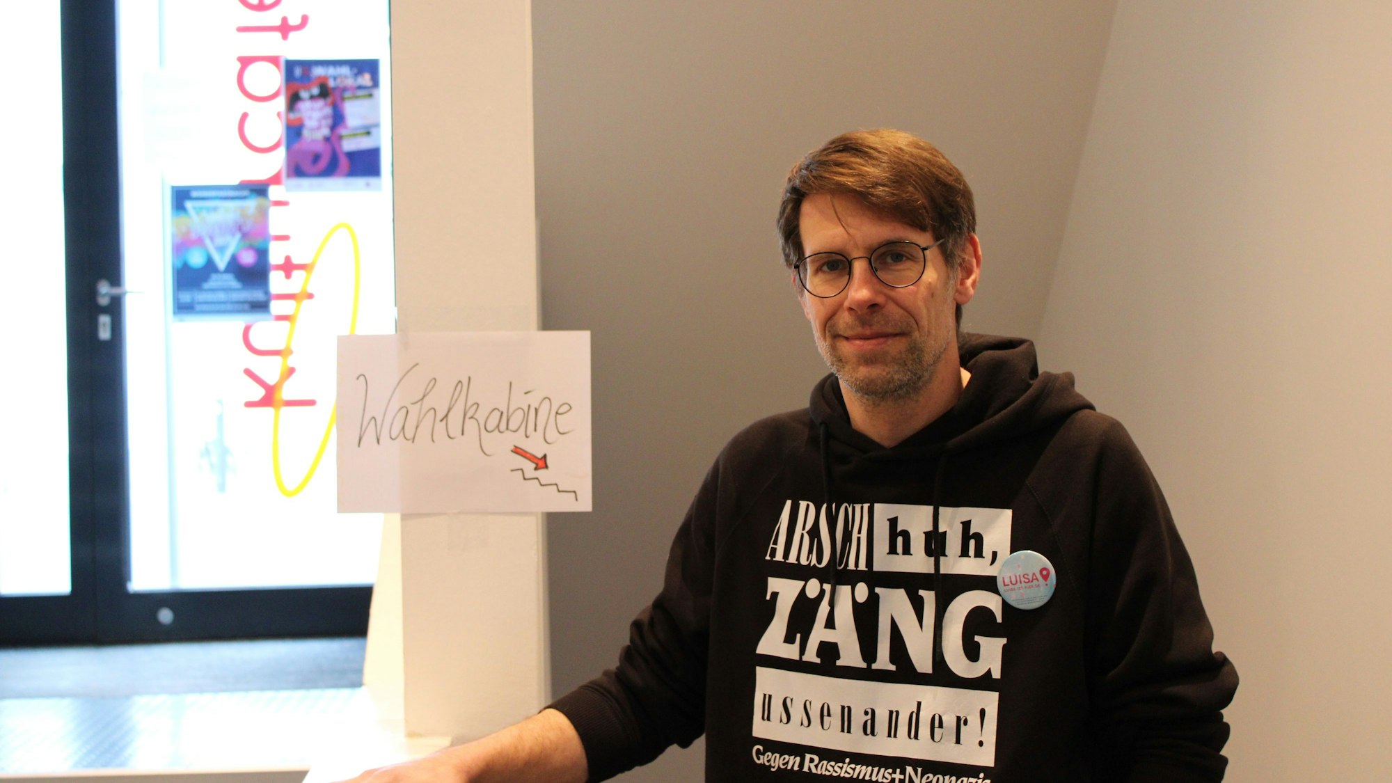 Ein Mann steht im Eingangsbereich des Siegburger Kulturcafés, im Hintergrund ist ein Schild mit der Aufschrift „Wahlkabine“ zu sehen.