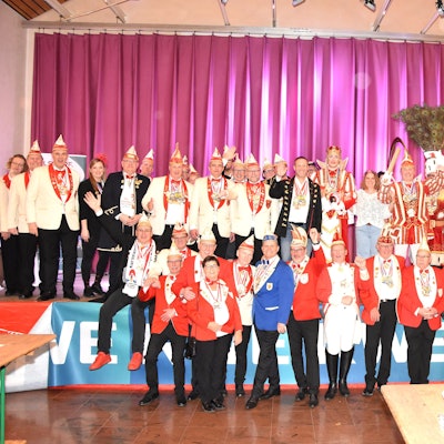 Auf dem Bild ist die Karnevalsgesellschaft in roten, blauen, weißen und schwarzen Trachten und spitzen Mützen zu sehen.