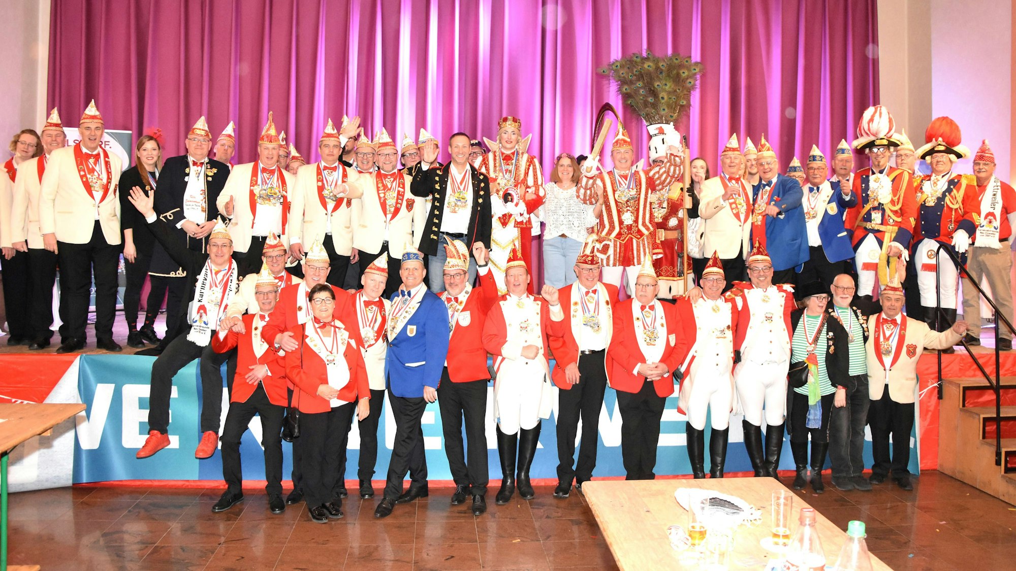 Auf dem Bild ist die Karnevalsgesellschaft in roten, blauen, weißen und schwarzen Trachten und spitzen Mützen zu sehen.