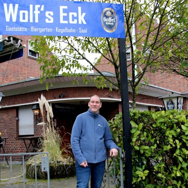 Auf dem Bild ist ein Mann vor einer Gaststätte zu sehen.