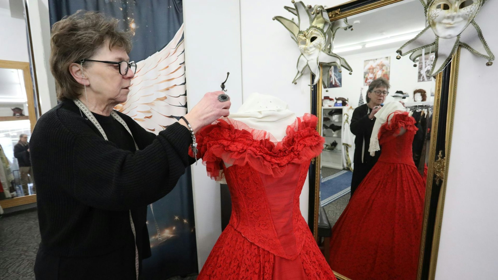 Eine Frau arbeitet an einem festlichen roten Kleid, das vor einem großen Spiegel steht.