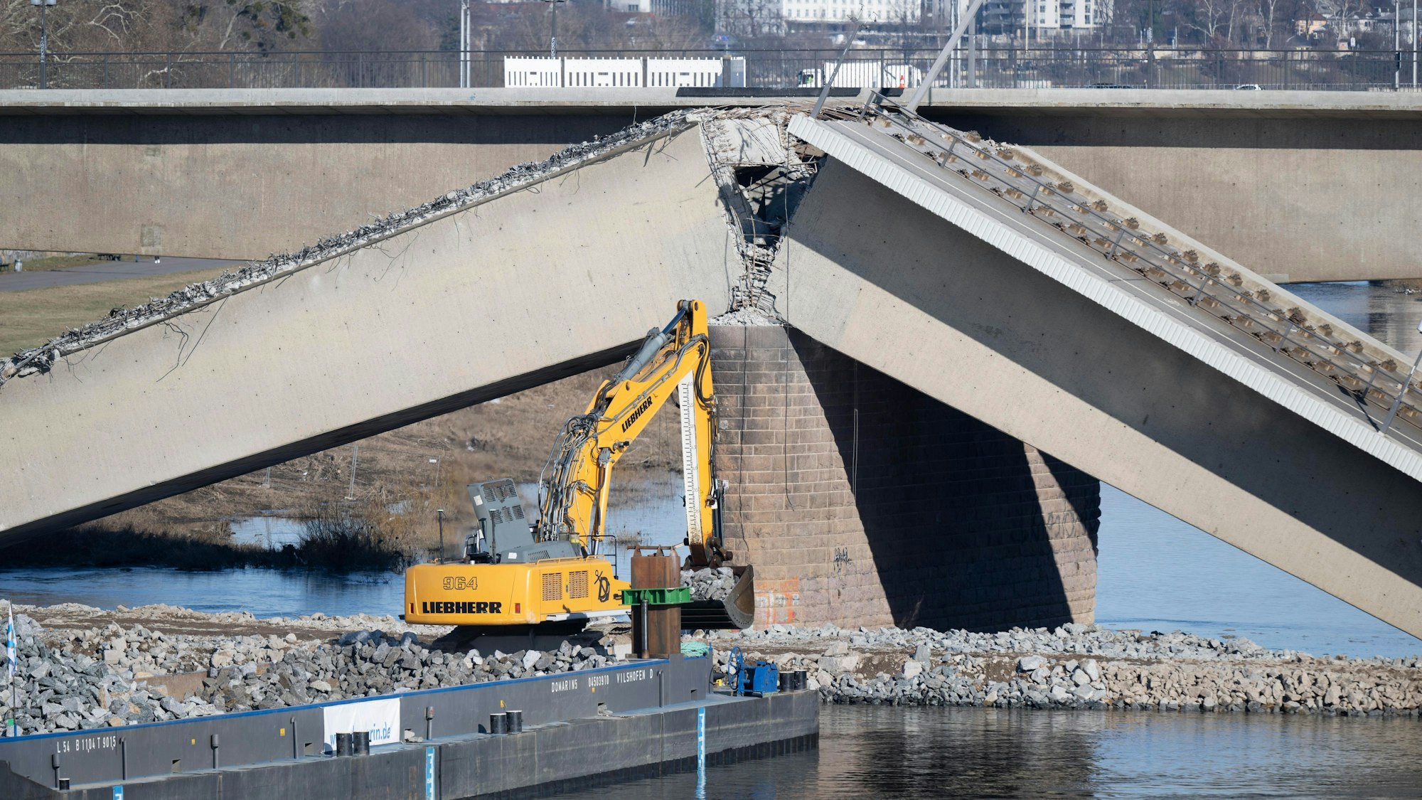 18.02.2025, Sachsen, Dresden: Ein auf einem Schiff stehender Bagger auf der Neustädter Elbseite arbeitet am eingestürzten Brückenzug der Carolabrücke. Die Abrissarbeiten an der eingestürzten Dresdner Carolabrücke sind wegen weiterer Brüche in der Konstruktion vorerst eingestellt. Foto: Sebastian Kahnert/dpa +++ dpa-Bildfunk +++