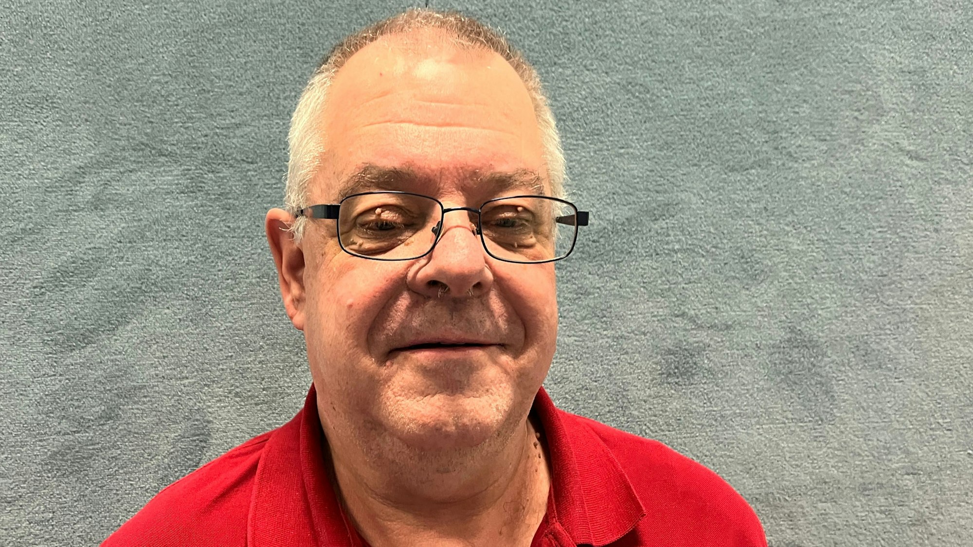 Ein Mann im roten T-Shirt steht vor einer Wand.