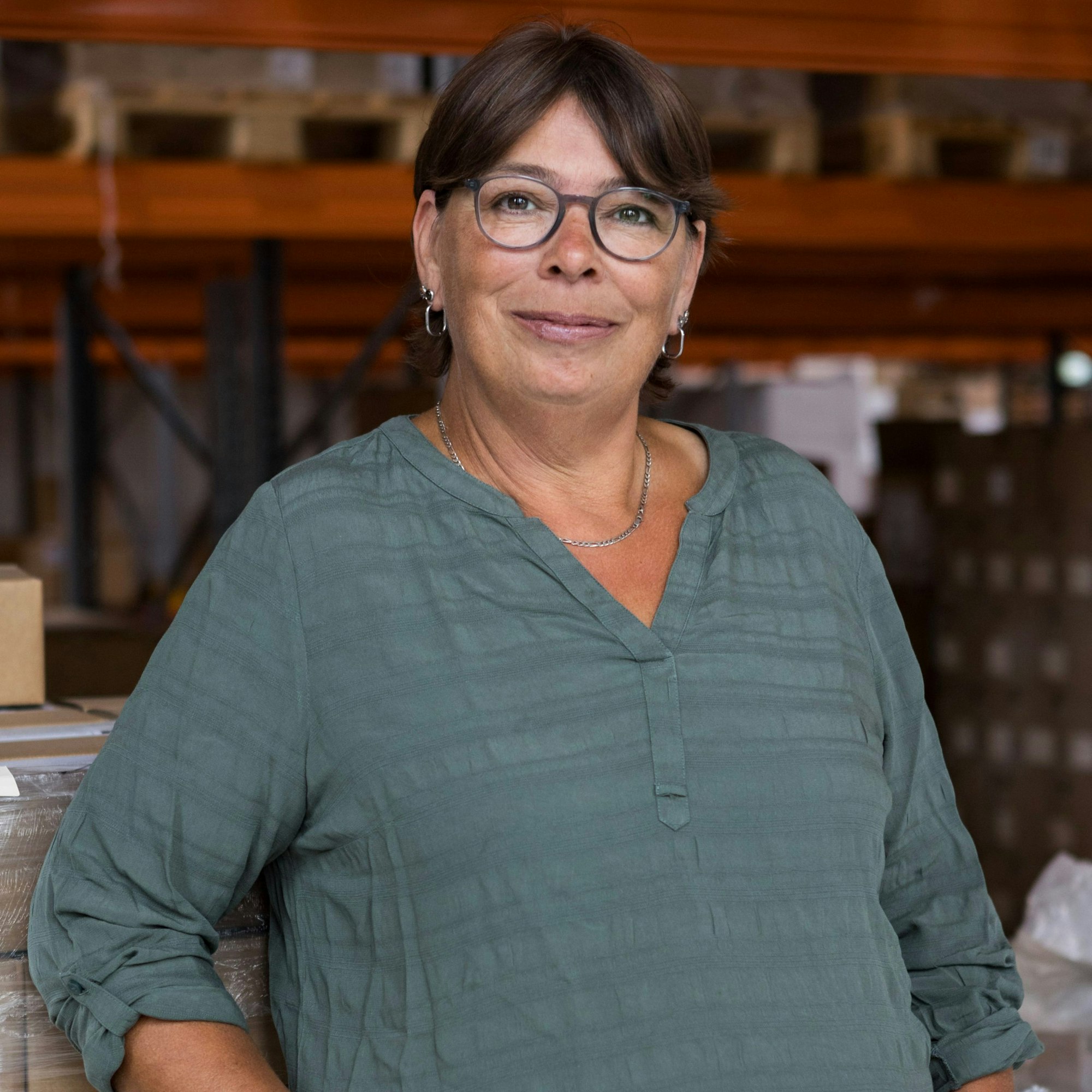 Eine Frau mit braunen Haaren und grün-blauer Bluse lächelt in die Kamera.