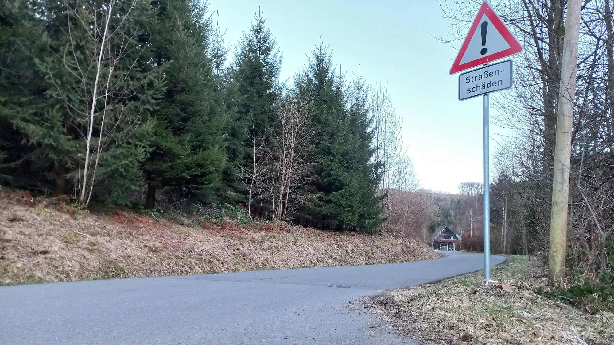 Blick auf eine Straße mit einem Schild, das vor Straßenschäden warnt.