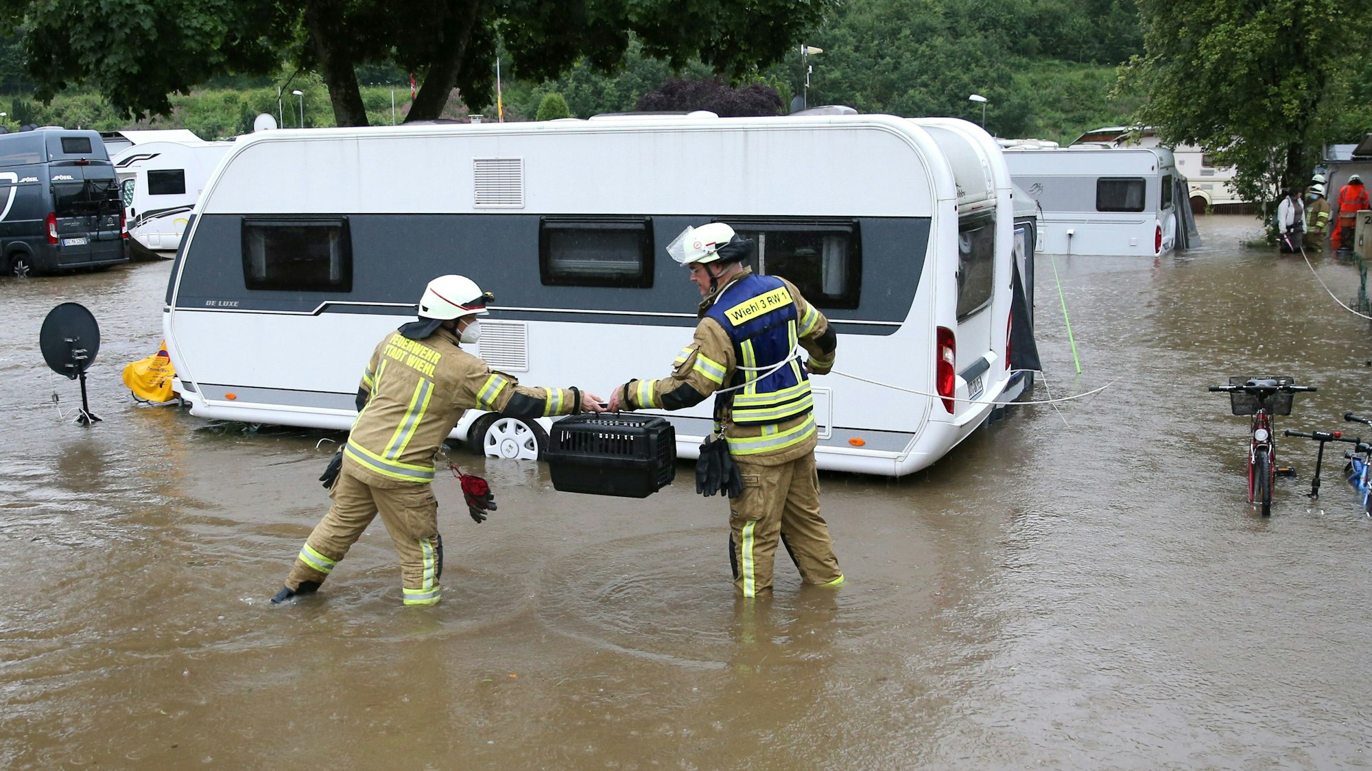 Feuerwehrleute stehen auf einem überfluteten Campingplatz.