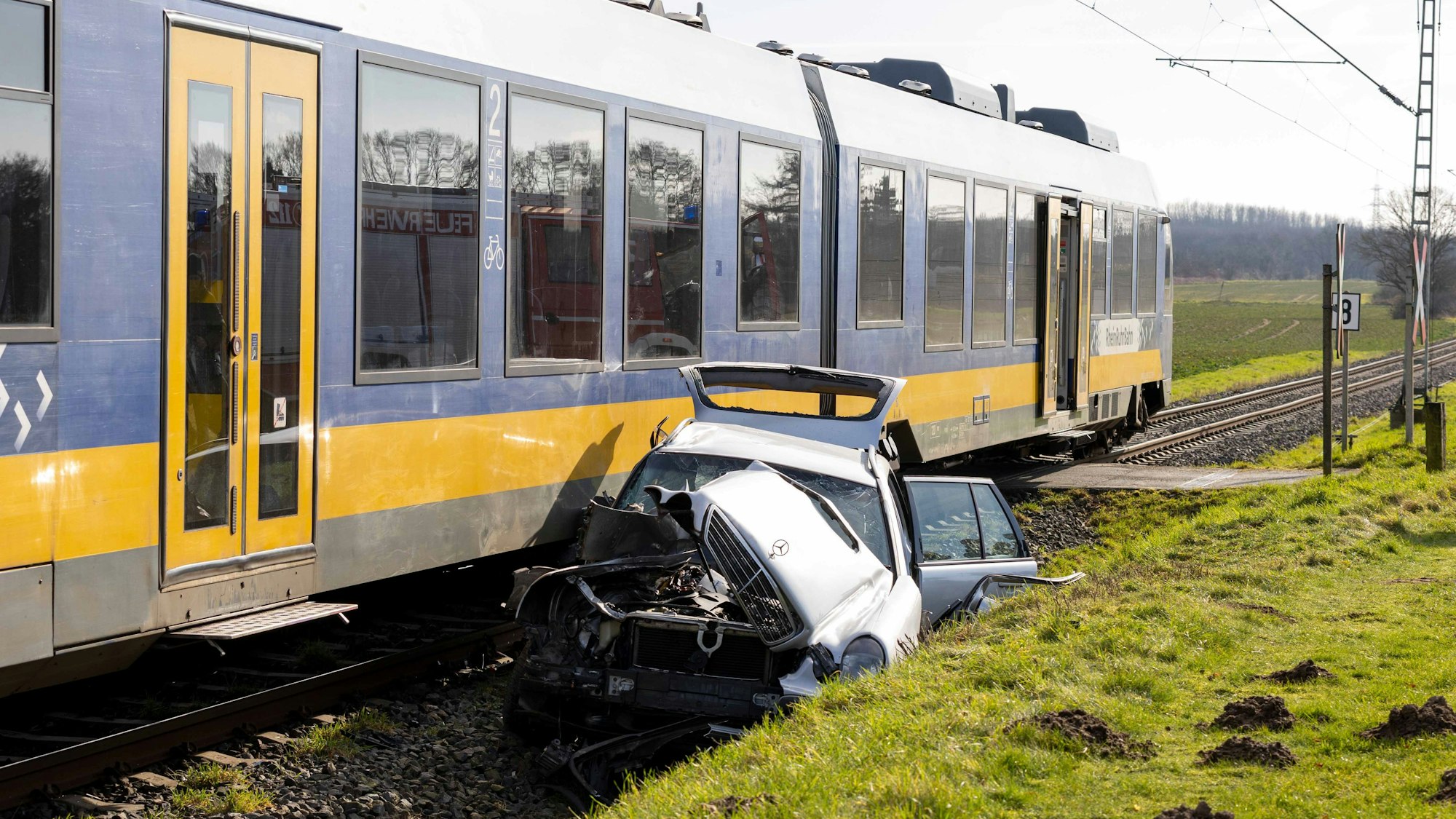 Ein zerstörter Mercedes liegt neben einer Regionalbahn.