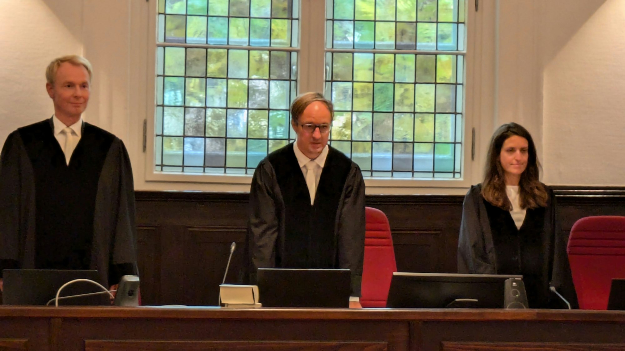 Zwei Richter und eine Richterin stehen nebeneinander. Sie tragen schwarze Roben.