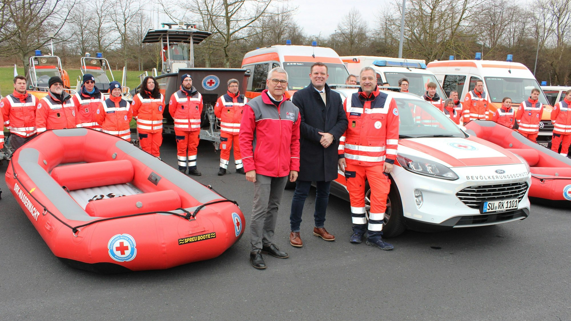 Mitglieder der Wasserwacht des Deutschen Roten Kreuzes stehen vor einem neuen Fahrzeug und einem Raft, einem Schlauchboot.