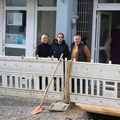 Drei Menschen hinter Speerbaken einer Baustelle, die nur wenig Platz zu den Ladenlokalen lassen.