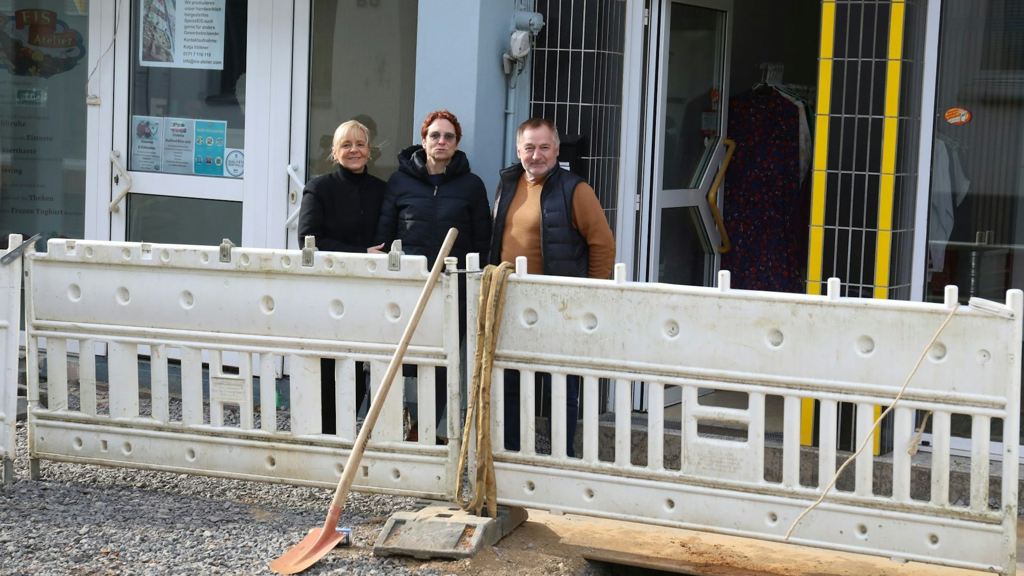 Drei Menschen hinter Speerbaken einer Baustelle, die nur wenig Platz zu den Ladenlokalen lassen.