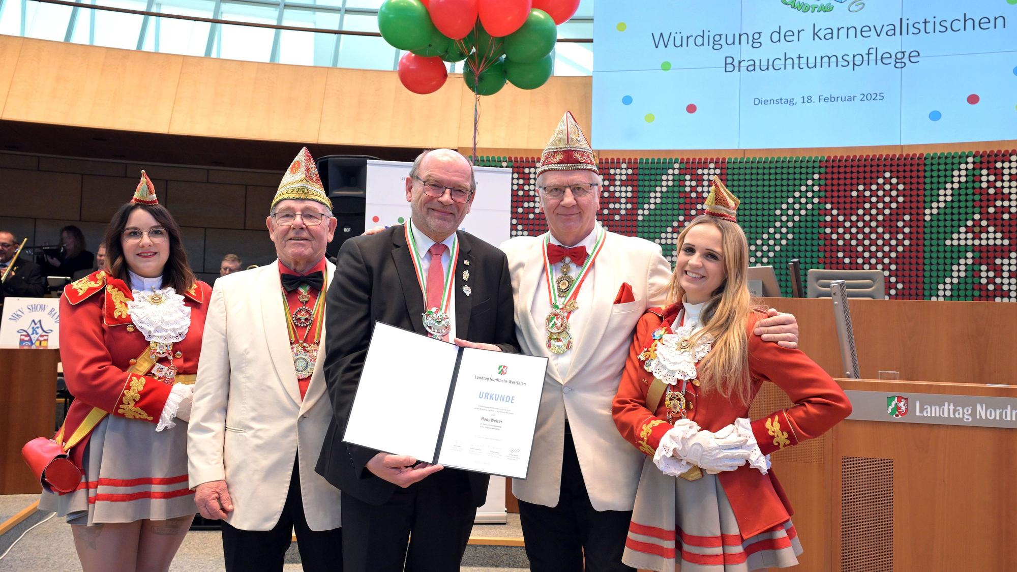 Landtagspräsident André Kuper überreicht Hans-Josef Welter im Beisein weiterer Mitglieder eines Karnevalsvereins eine Urkunde und einen Orden.