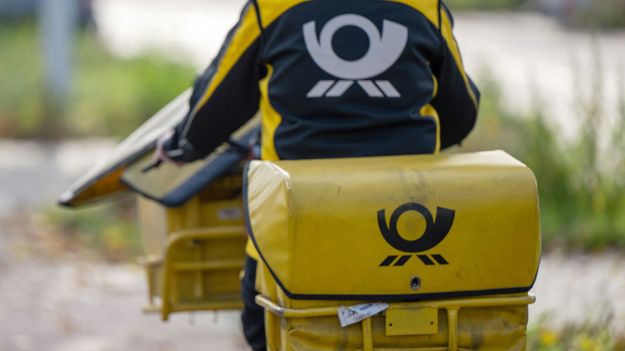 Eine Postbotin in Uniform auf dem Fahrrad von hinten