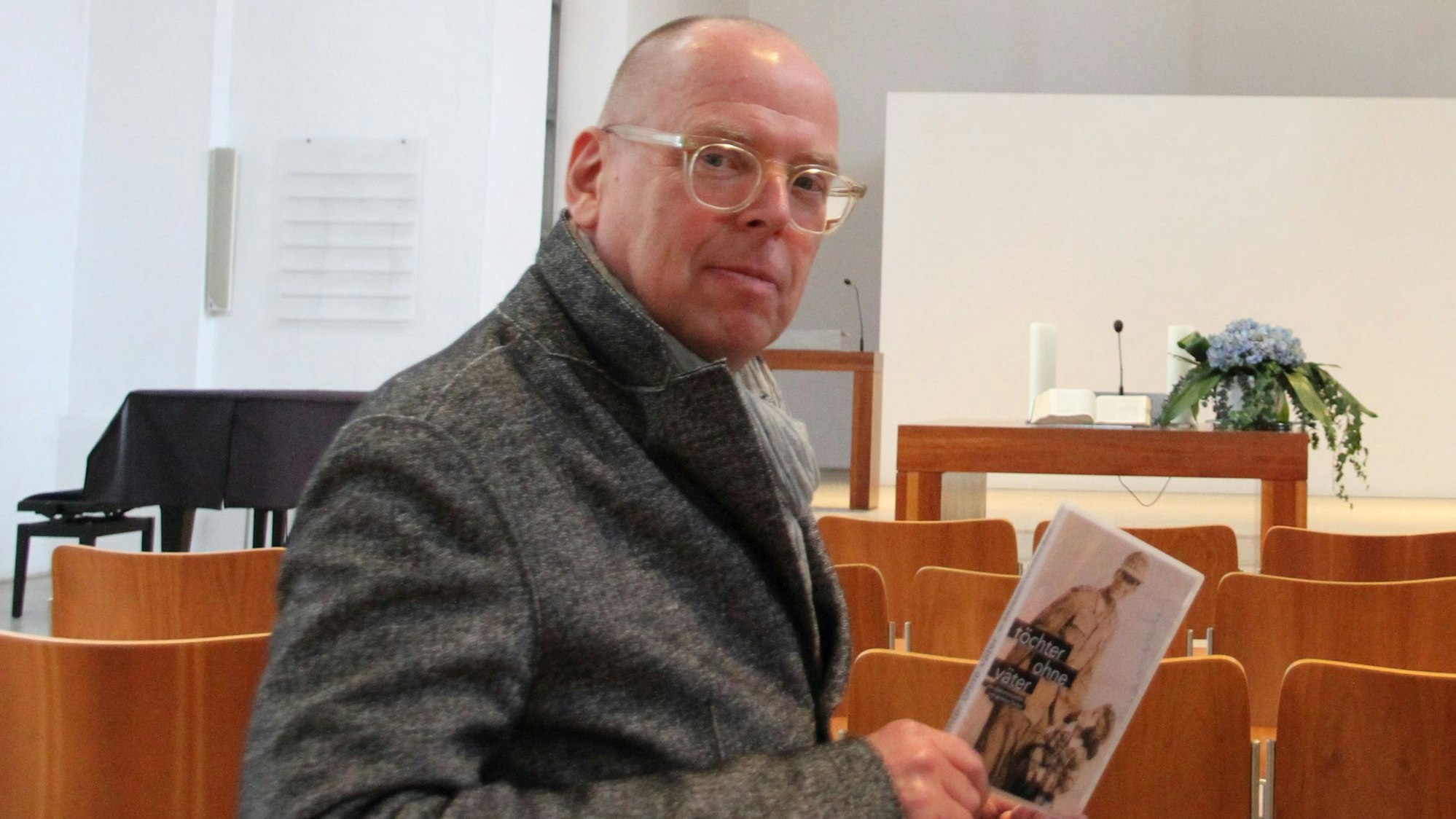 Ein Mann mit Glatze und Brille sitzt in einem Kirchenraum.