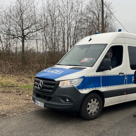 Ein Einsatzfahrzeug der Polizei steht auf einer Straße, ein Polizist steht daneben.