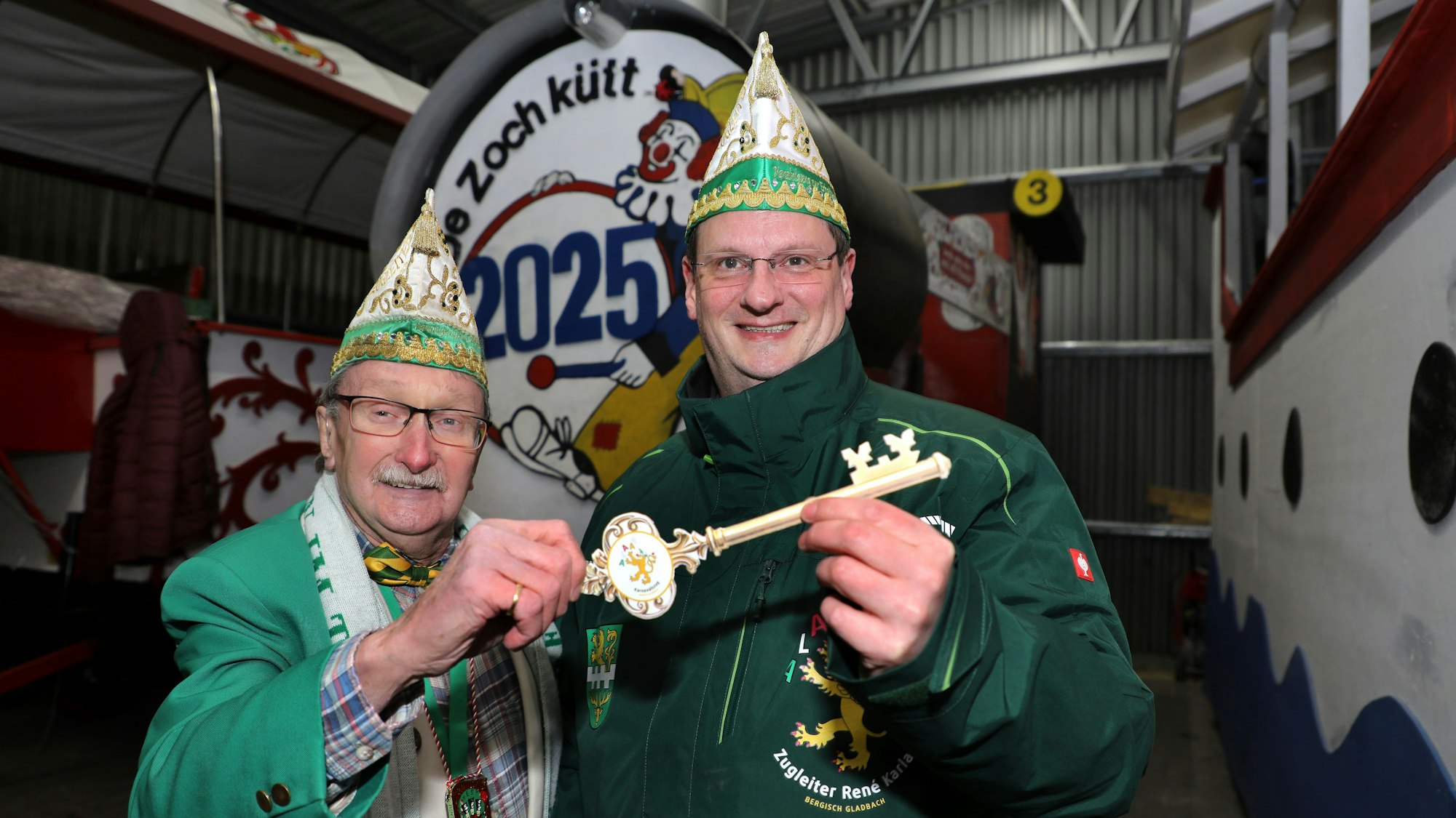 Helmut Kraus und sein Nachfolger als Zugleiter, René Karla, stehen mit einem großen Schlüssel vor der Zugleiter-Lokomotive des Bergisch Gladbacher Karnevalszugs.