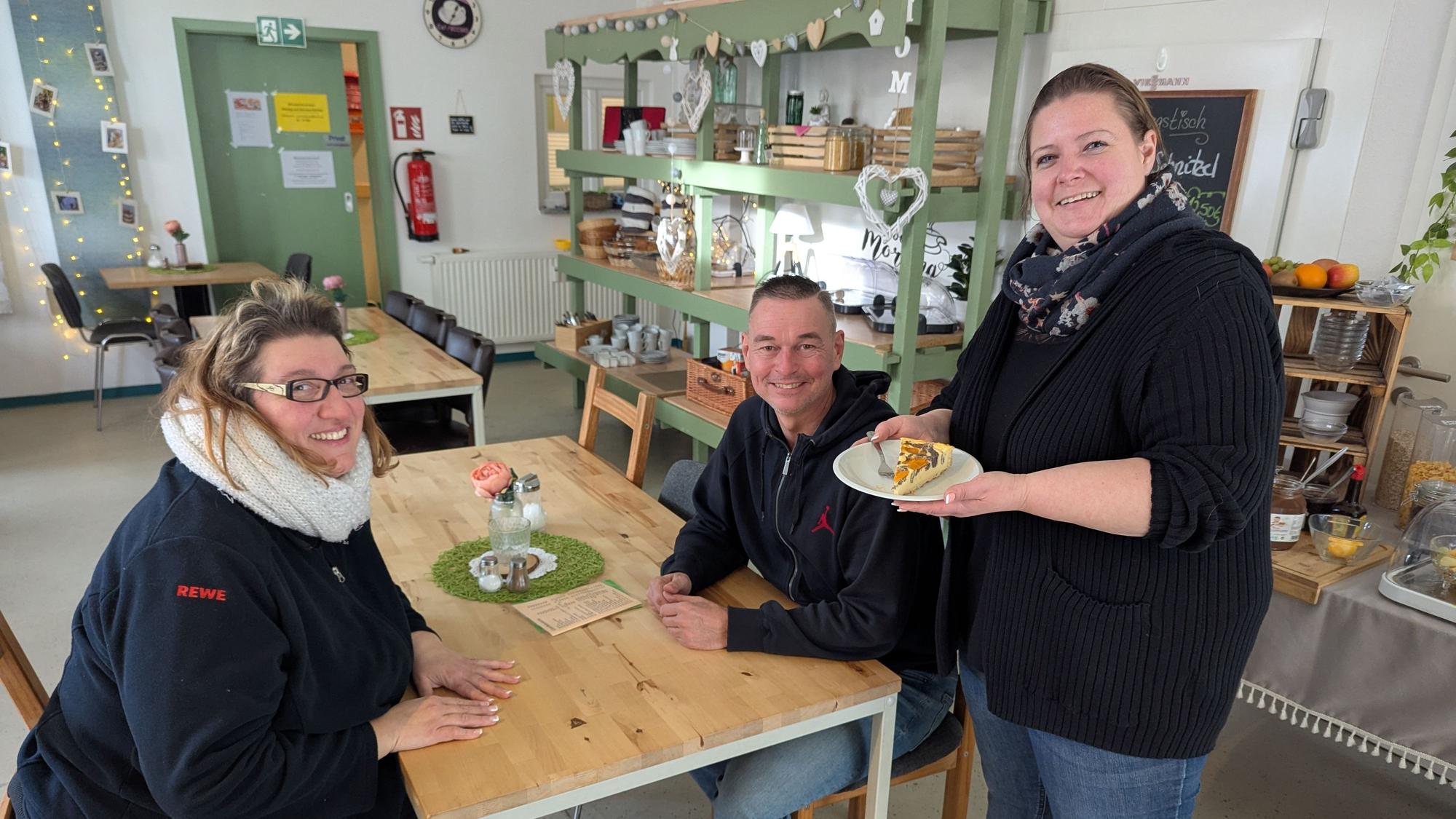 Das Foto zeigt die Inhaberin, die Gästen im Café ein Stück Kuchen bringt.