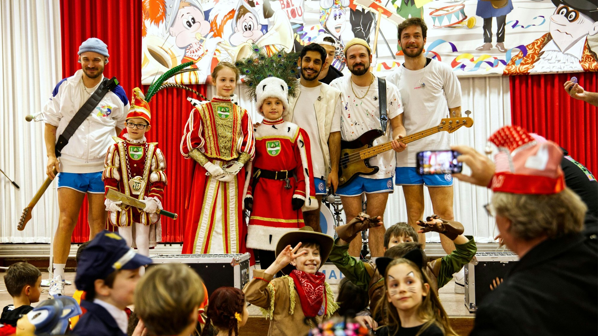 Ein Kinderdreigestirn steht mit vier jungen Männern auf einer Karnevalsbühne