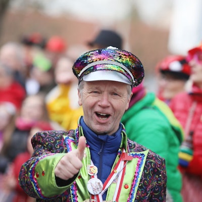 Ein Mann im bunten Karnevalskostüm zeigt das „Daumen hoch“-Zeichen.