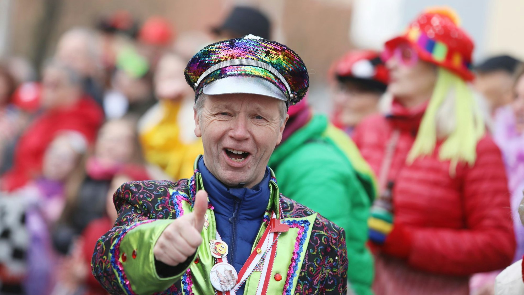 Ein Mann im bunten Karnevalskostüm zeigt das „Daumen hoch“-Zeichen.