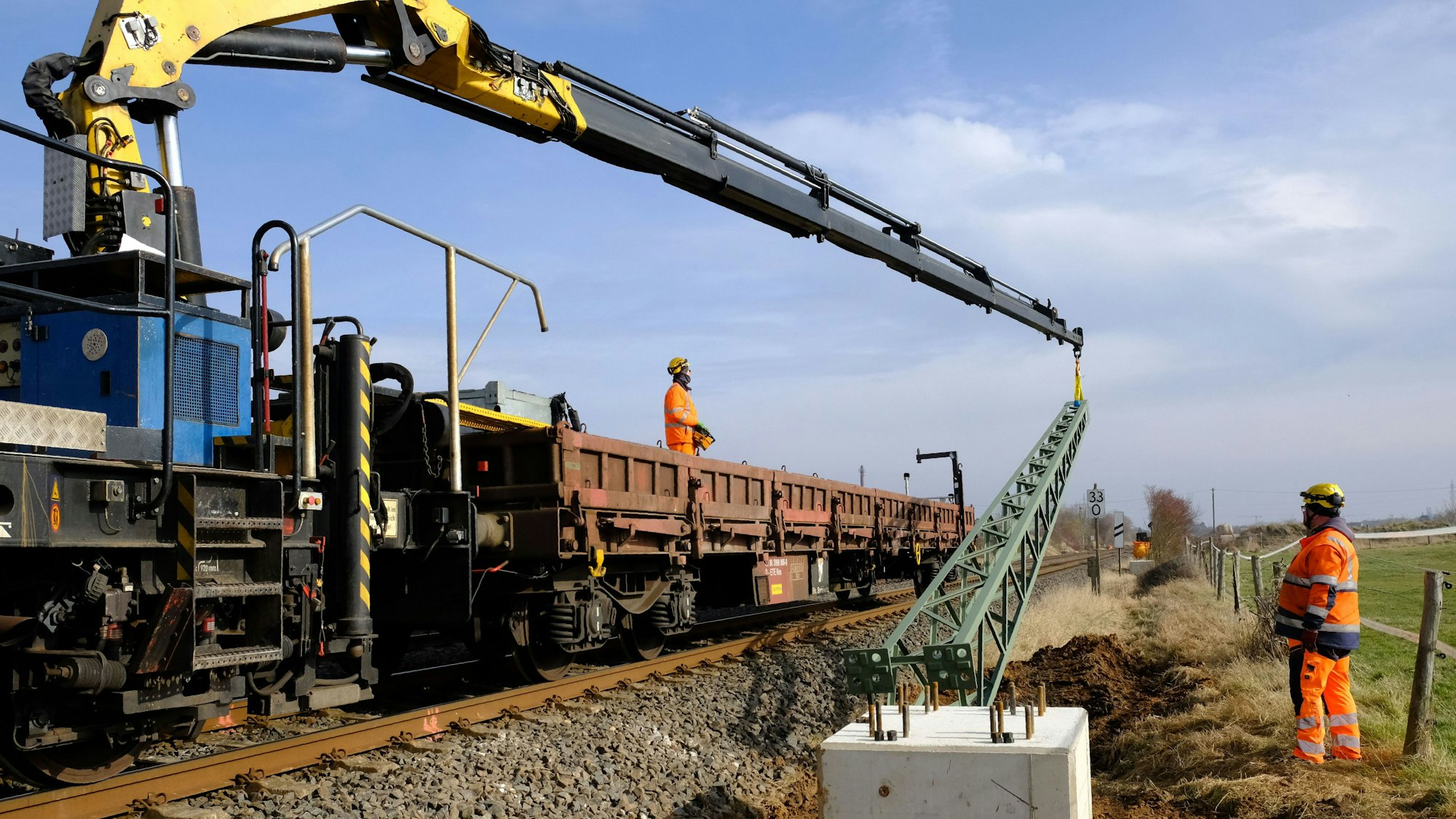 Mitarbeiter der Firma Europten montieren einen Oberleitungsmast auf einem Betonfundament.