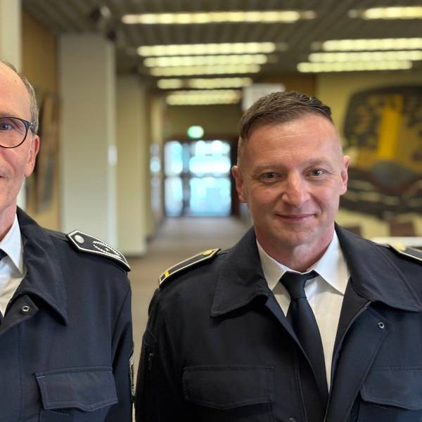 Auf dem Bild sind zwei Männer in Feuerwehruniform zu stehen, die in einem Flur des Frechener Rathauses stehen.