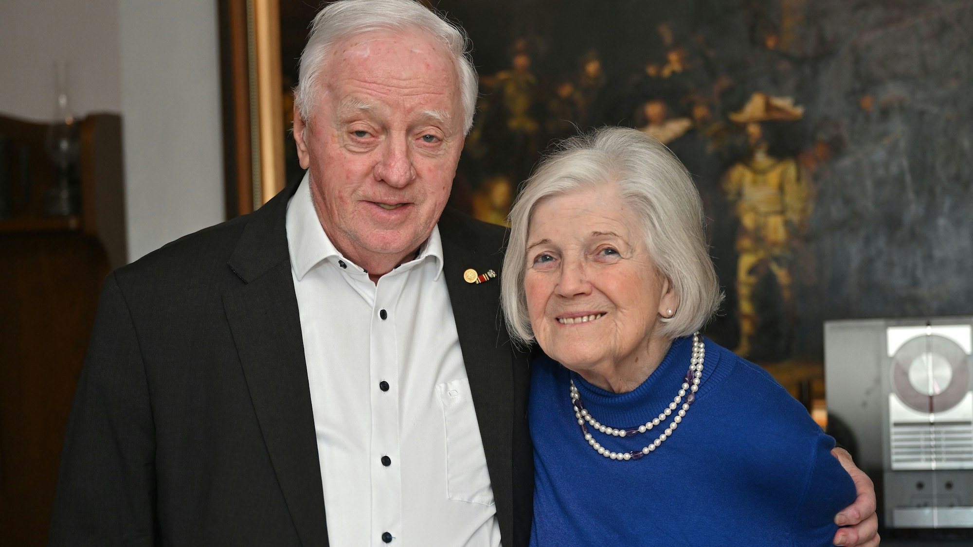 Das Paar steht nebeneinander. Er lebt den Arm um seine Frau.