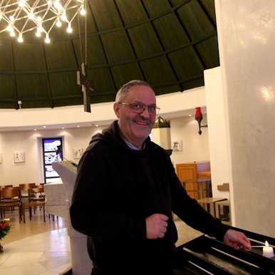 Auf dem Bild ist der Klinikseelsorger in schwarzer Kleidung in der Krankenhauskapelle zu sehen.