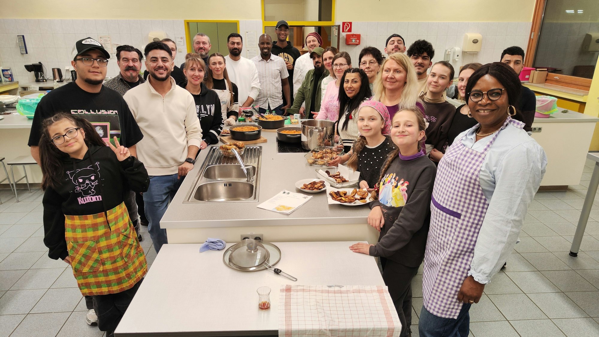 Die Teilnehmerinnen und Teilnehmer stehen um eine Kochinsel herum, auf der die fertige Speise angerichtet ist.