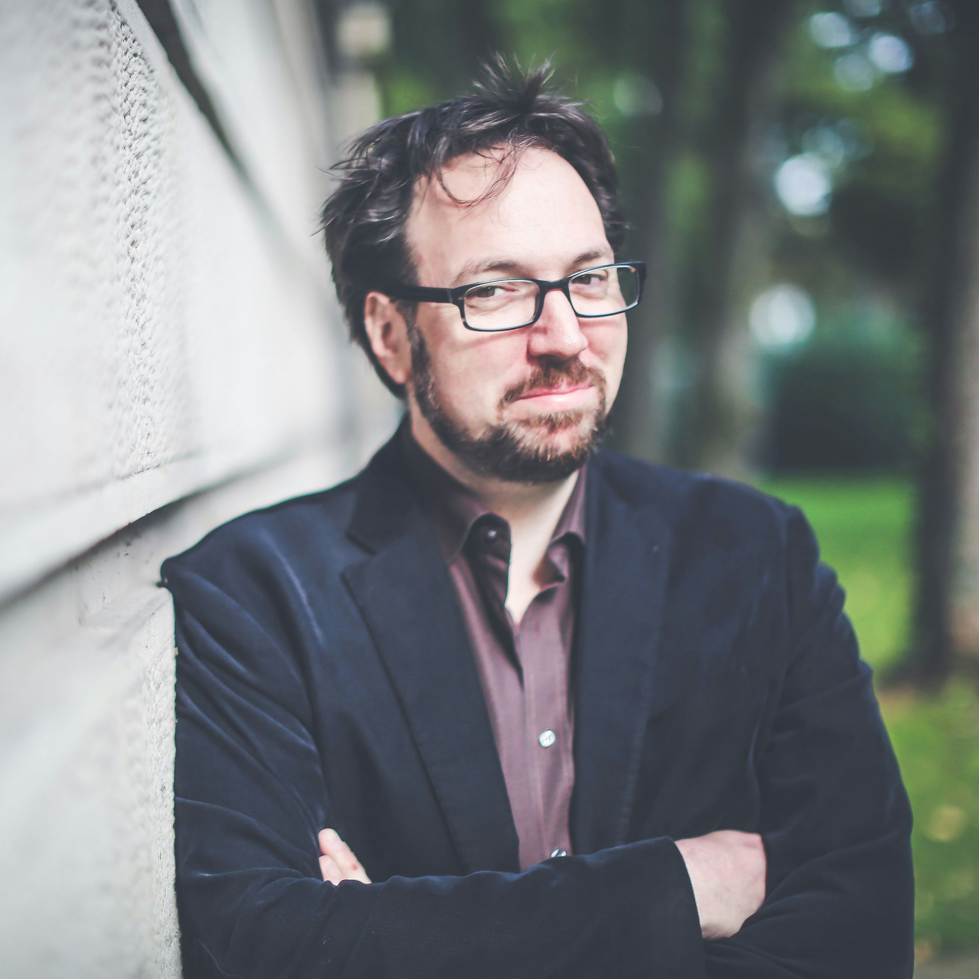 Ein Mann hat die Arme gekreuzt und lehnt an einer Wand.