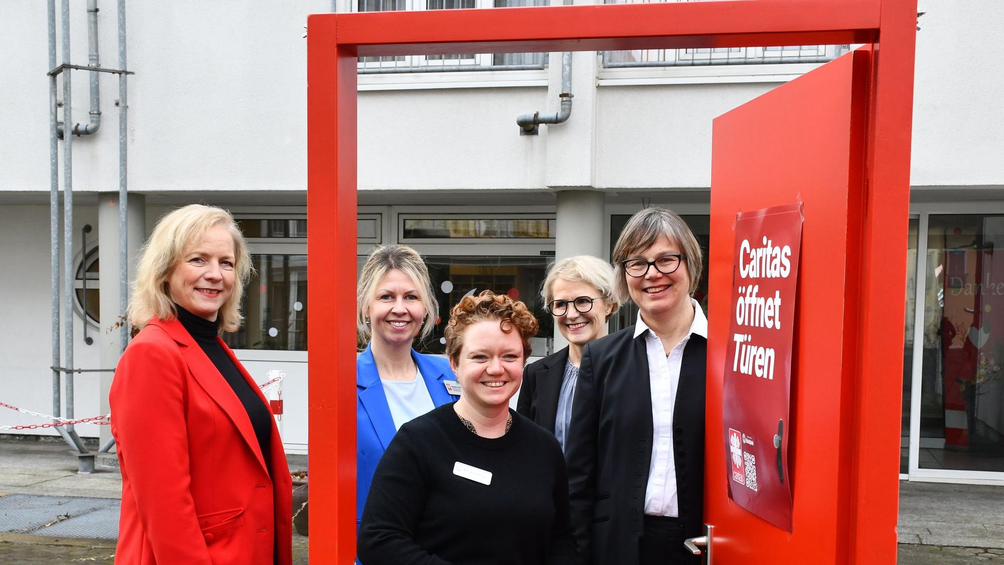 Das Foto zeigt das Führungsteam der Caritas vor einer geöffneten symbolischen roiten Tür.