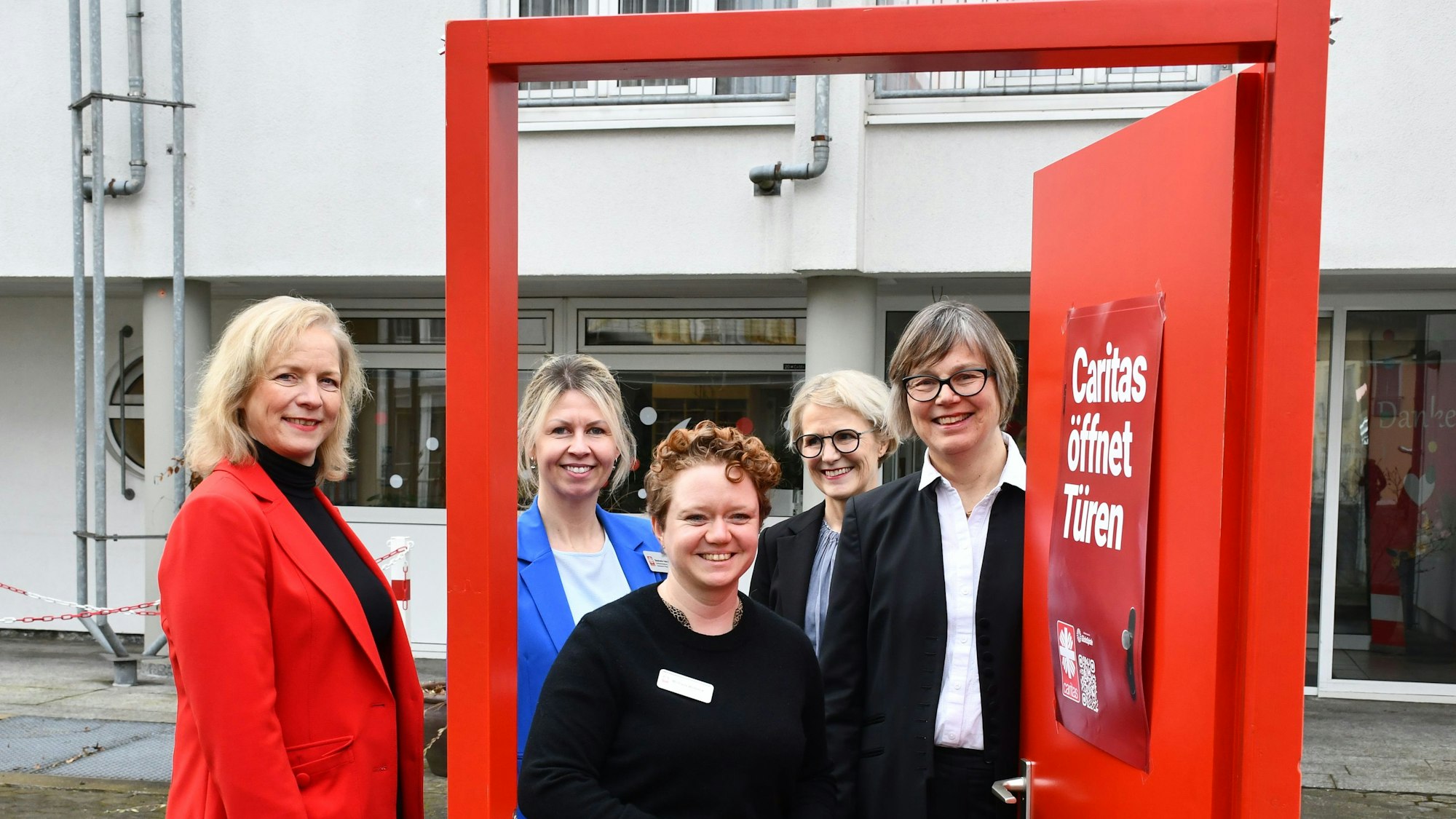 Das Foto zeigt das Führungsteam der Caritas vor einer geöffneten symbolischen roiten Tür.
