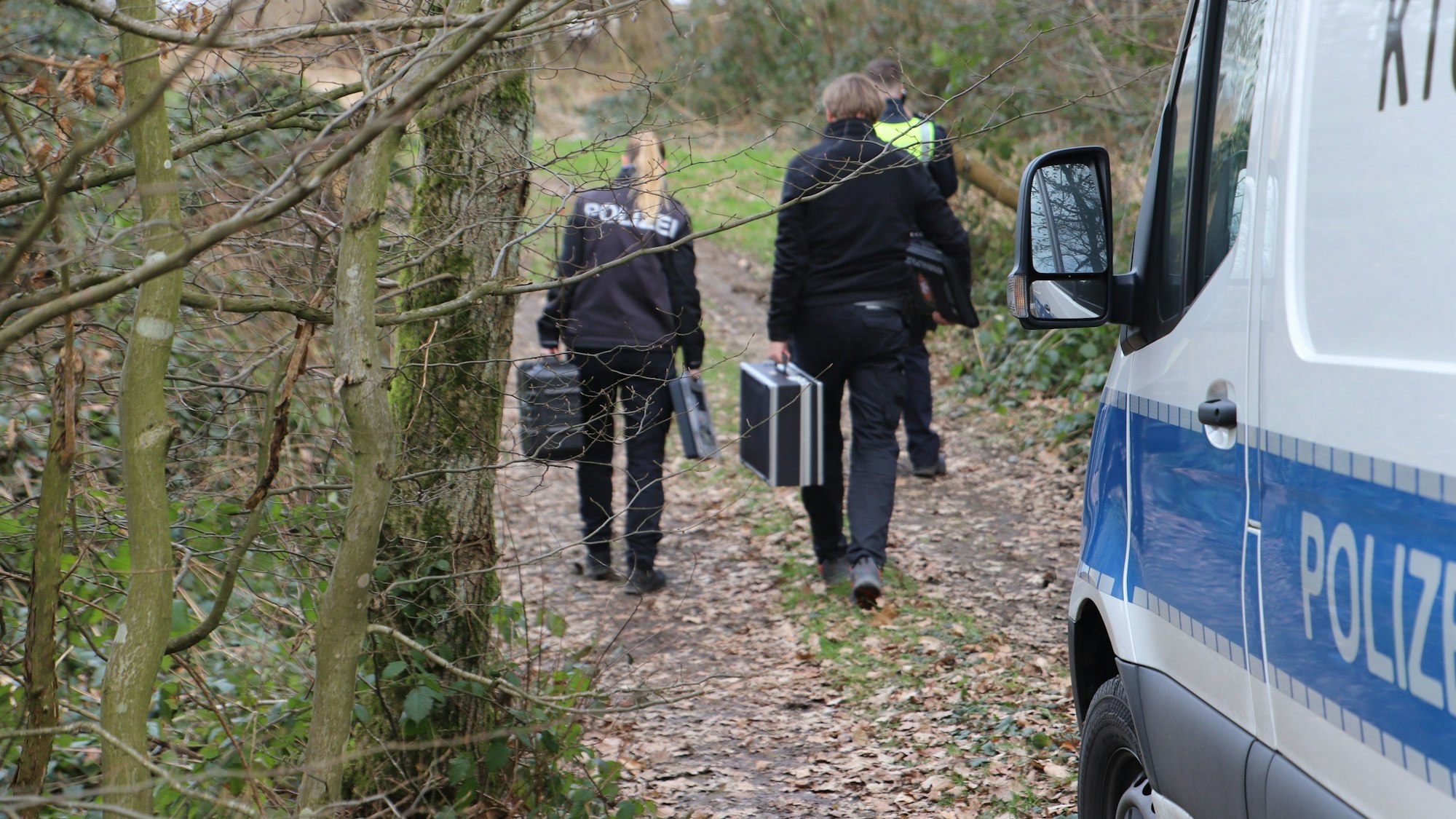 Der Polizisten gehen mit Koffern auf ein Grundstück.