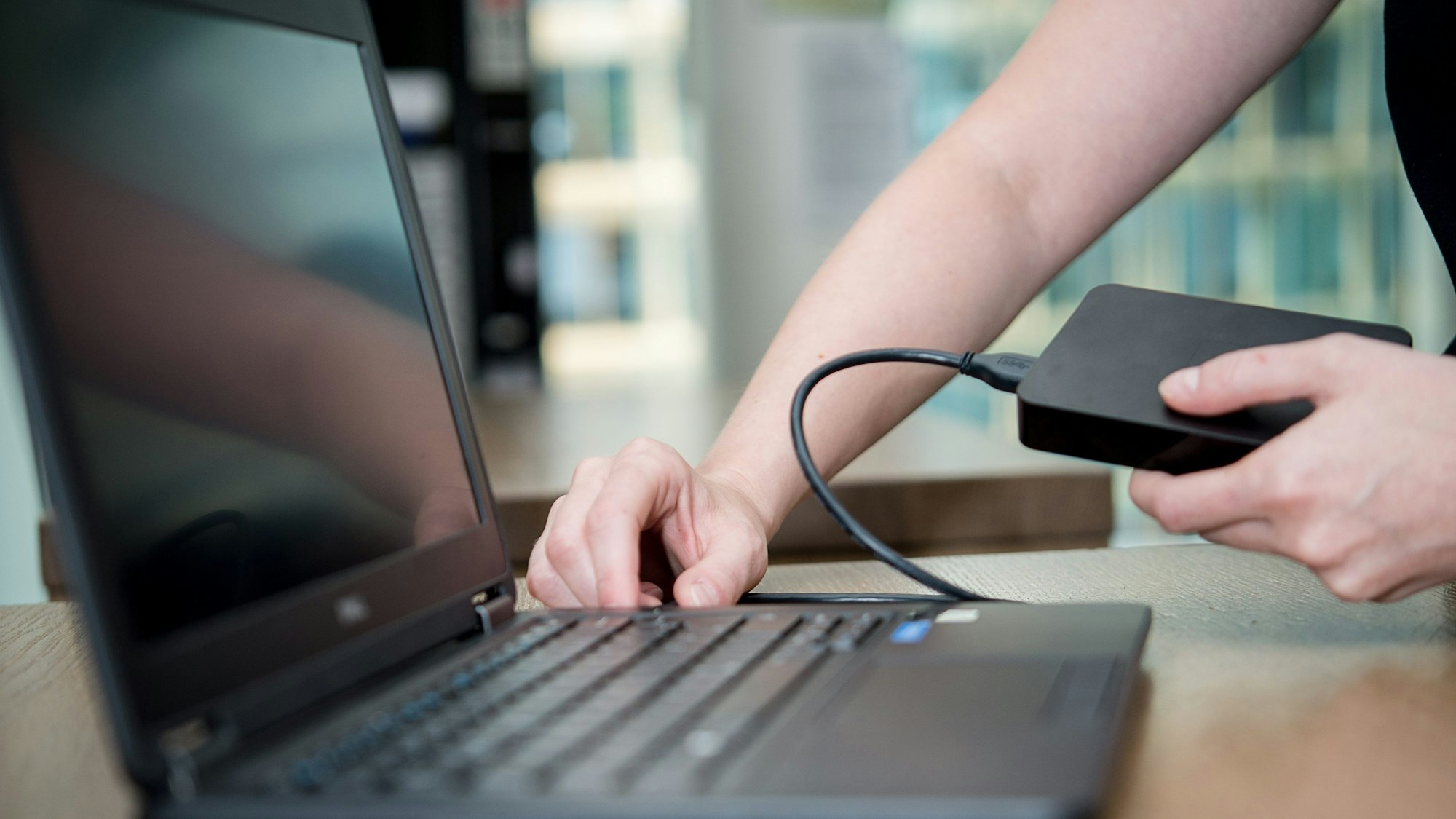Eine Person schließt eine externe Festplatte an einen Laptop an.