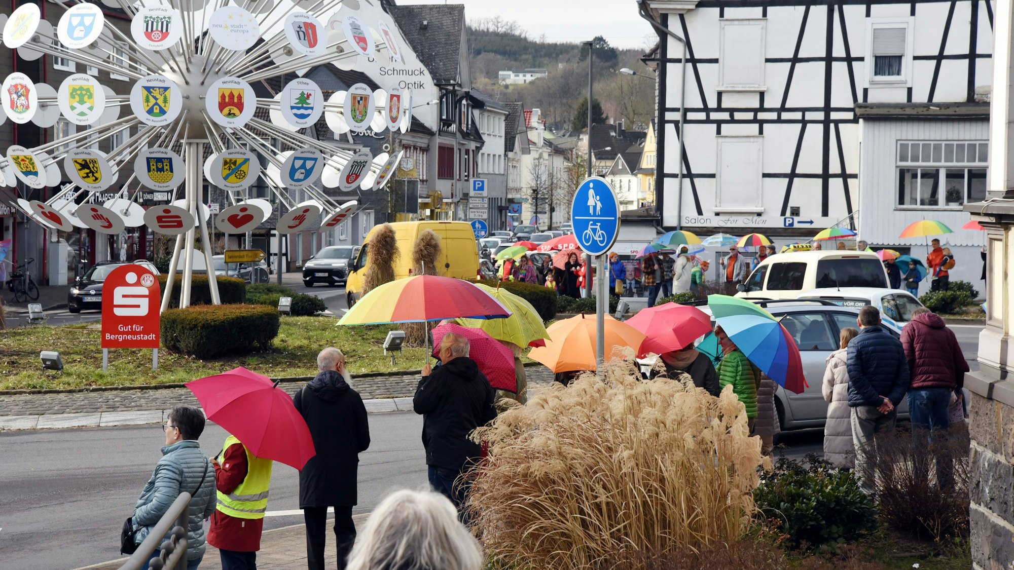 Menschen stehen mit Regenschirmen am Kreisverkehr.