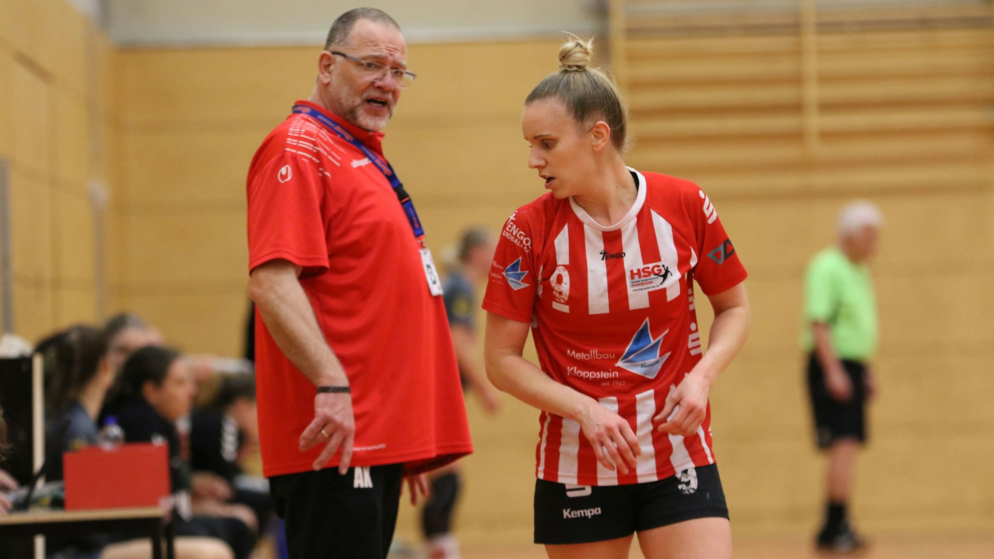 Der Trainer steht am Spielfeldrand, die Spielerin wendet den Kopf in seine Richtung.