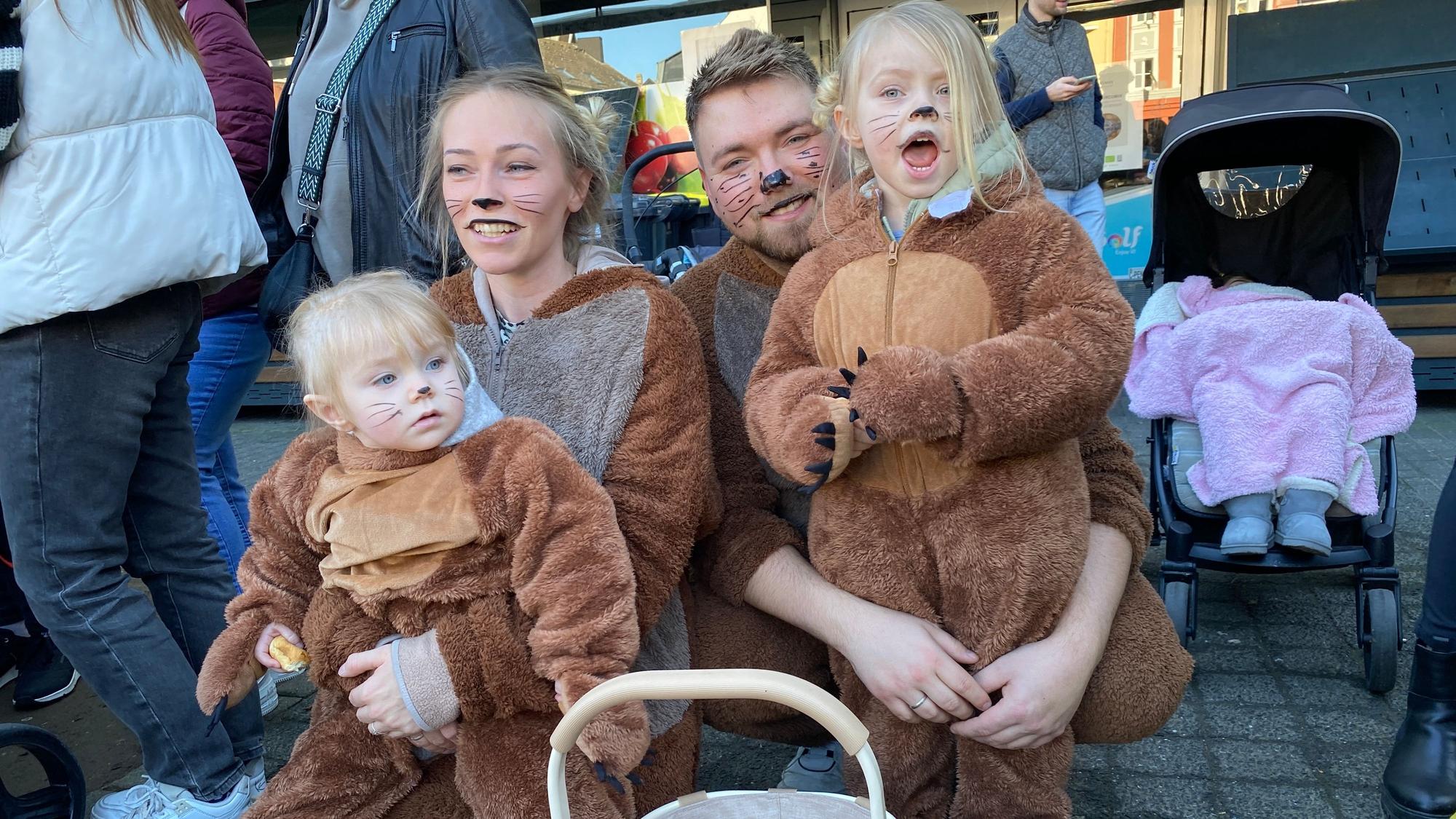 Mutter, Vater und zwei kleine Kinder in Bärenkostzümen hocken am Rand des Umzugs.