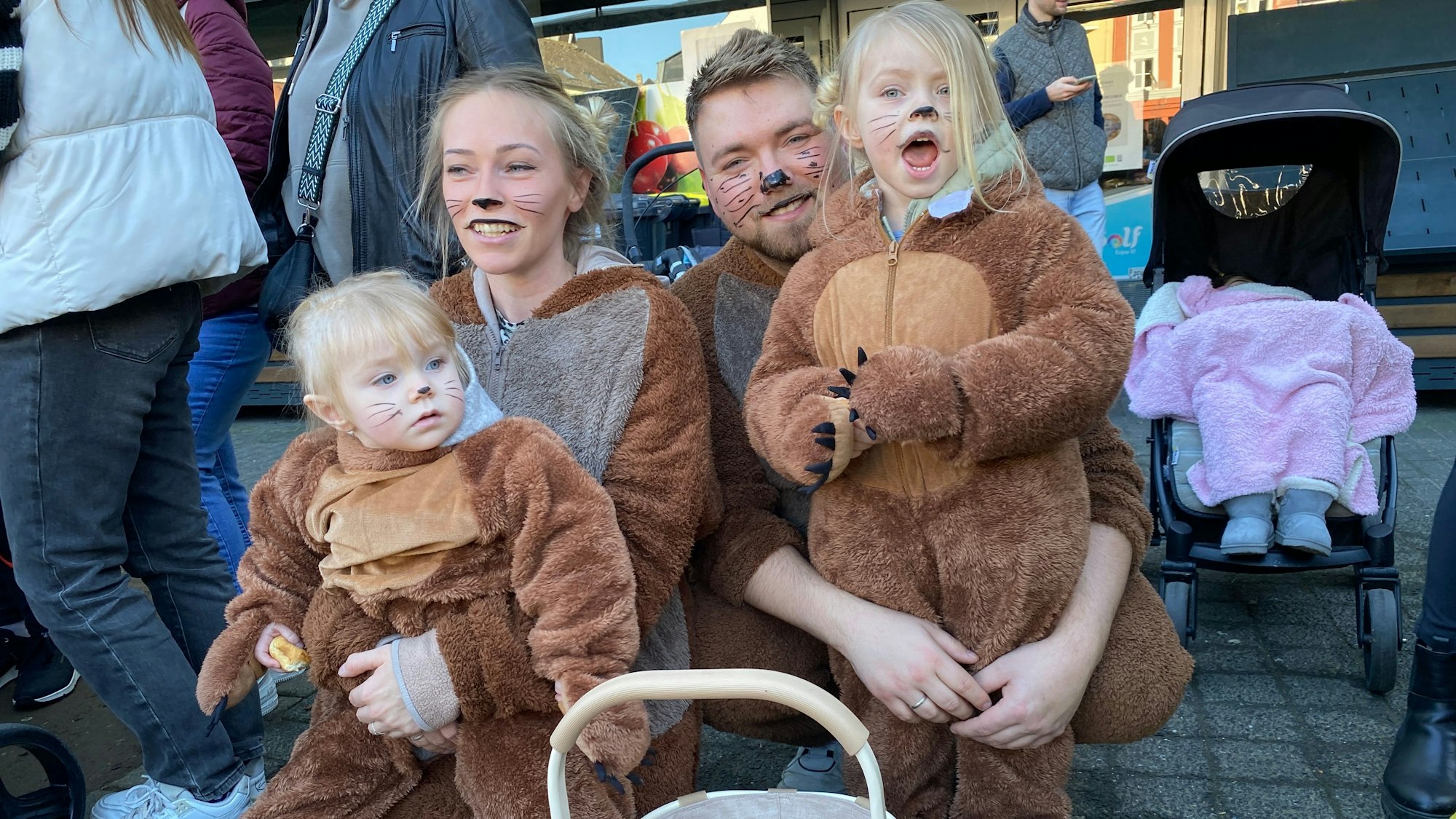 Mutter, Vater und zwei kleine Kinder in Bärenkostzümen hocken am Rand des Umzugs.