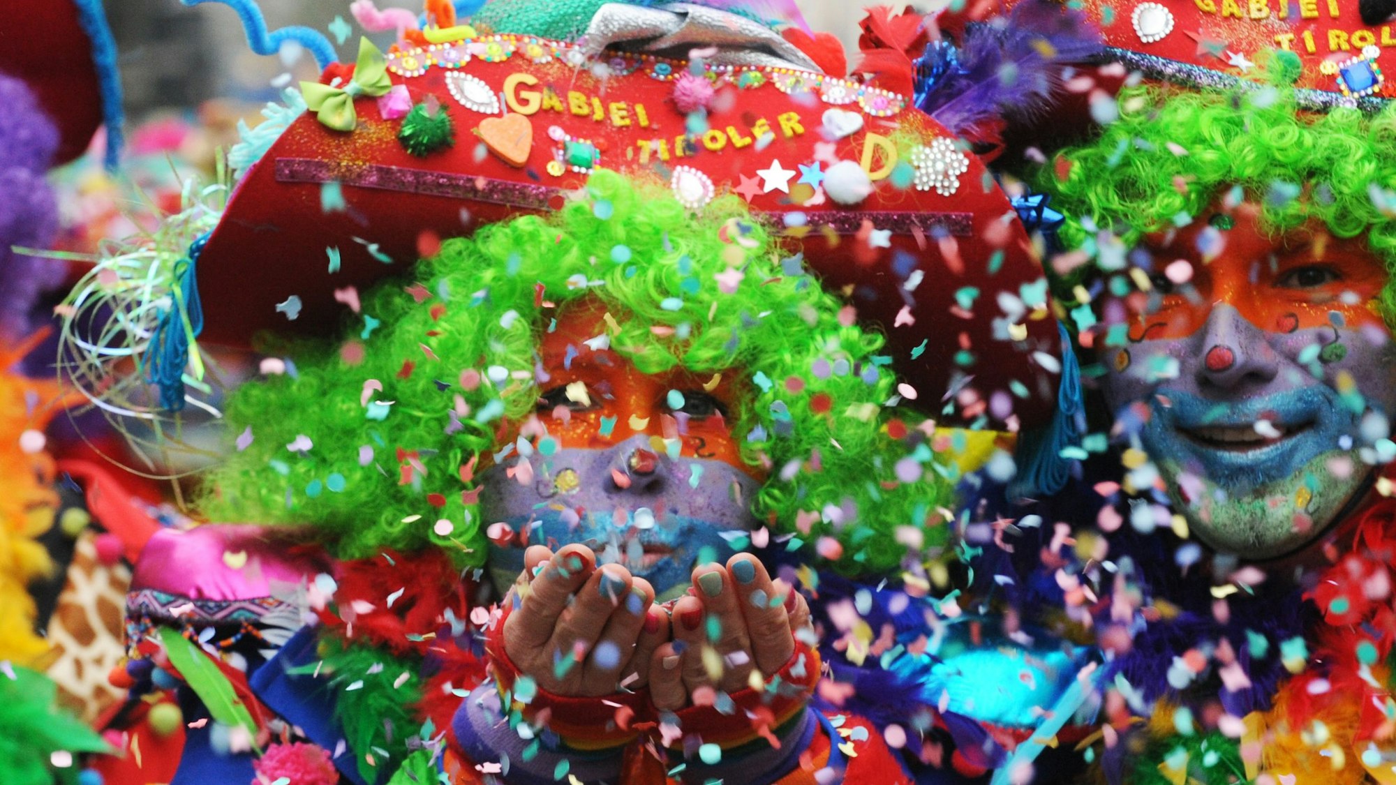 Das Foto zeigt bunt kostümierte Jecken, die Konfetti ins Publikum pusten.