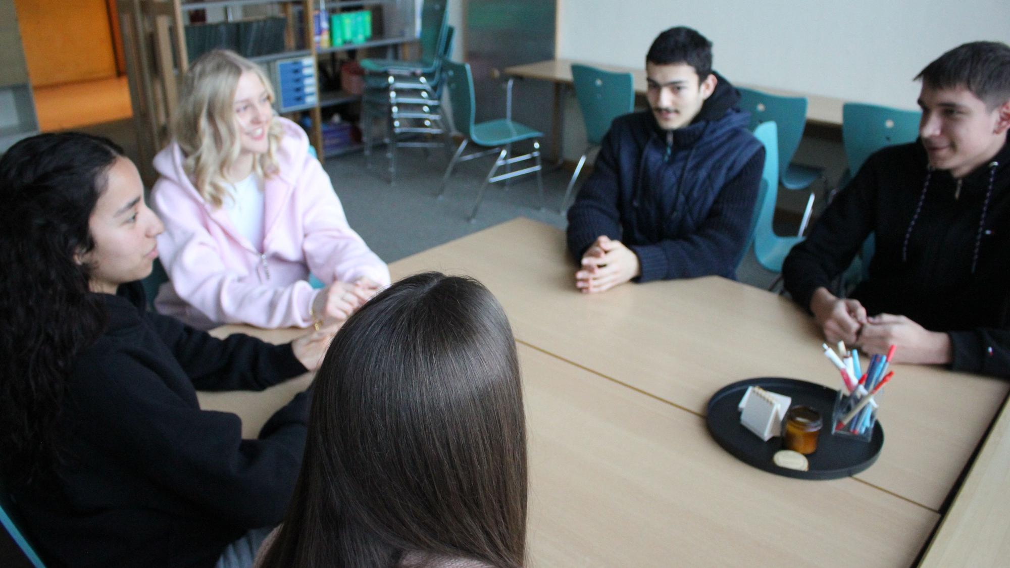 Zu sehen sind Julia, Jana, Mariame, Enes und Kaan, die an einem Tisch sitzen.