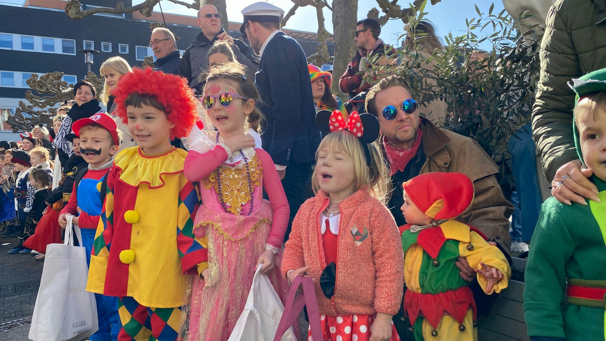Lustig kostümierte Kinder mit Beuteln in den Händen rufen am Zugrand nach Kamelle.