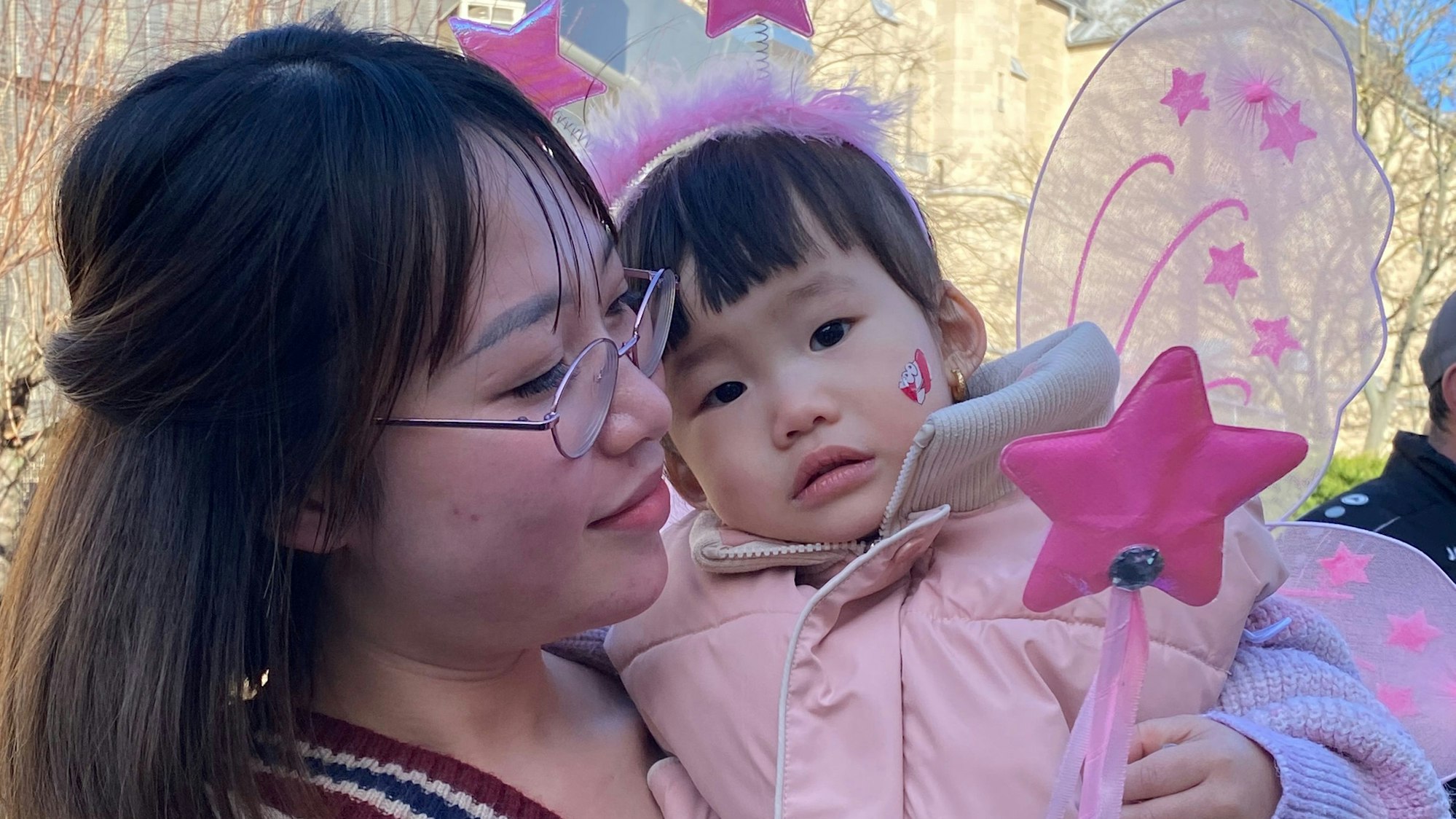 Ein kleines asiatisches Mädchen im Feenkostüm ist auf dem Arm ihrer Mutter.