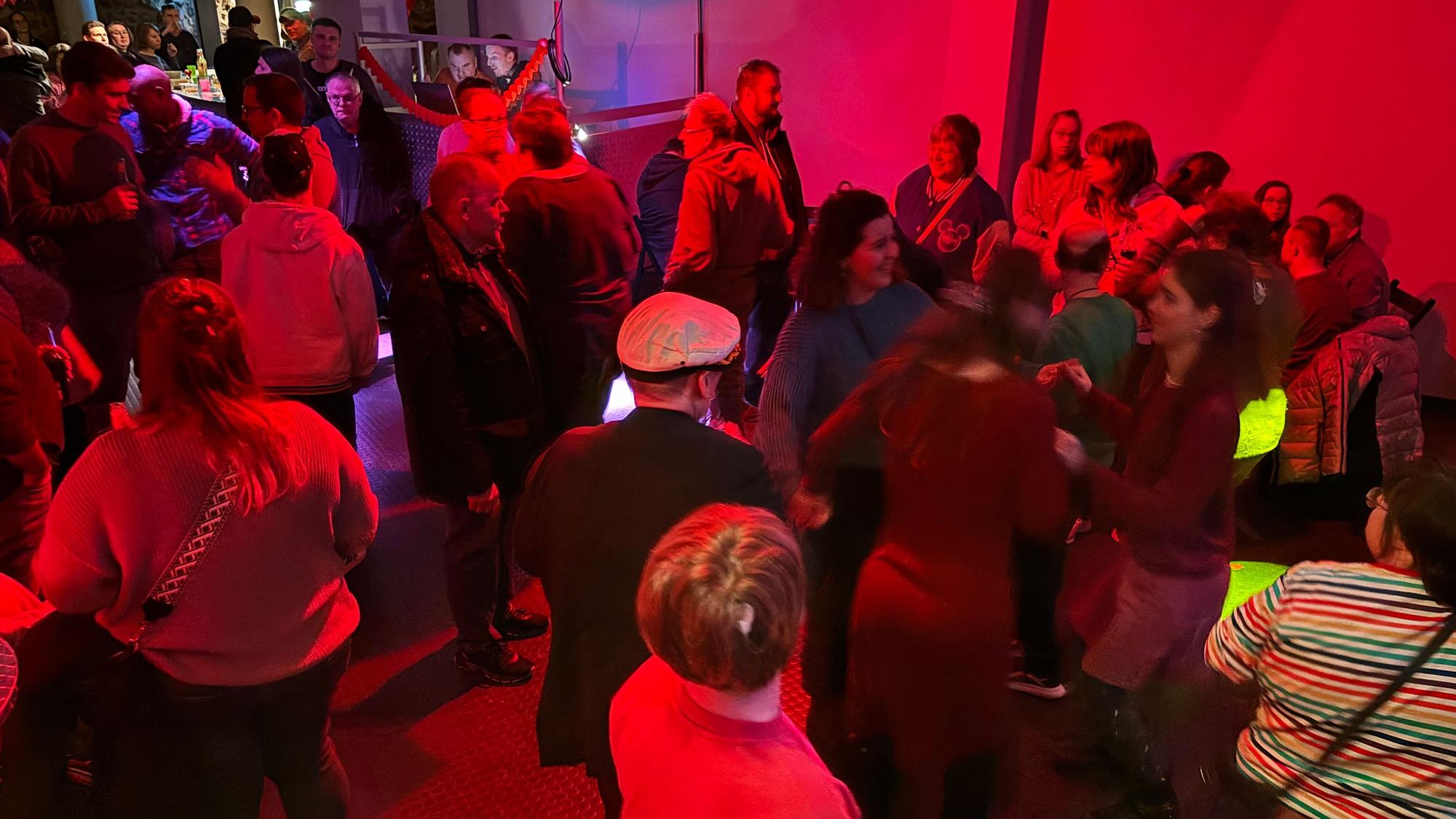 Mehrere Menschen tanzen in einem Raum, der mit einem roten Licht beleuchtet wird.