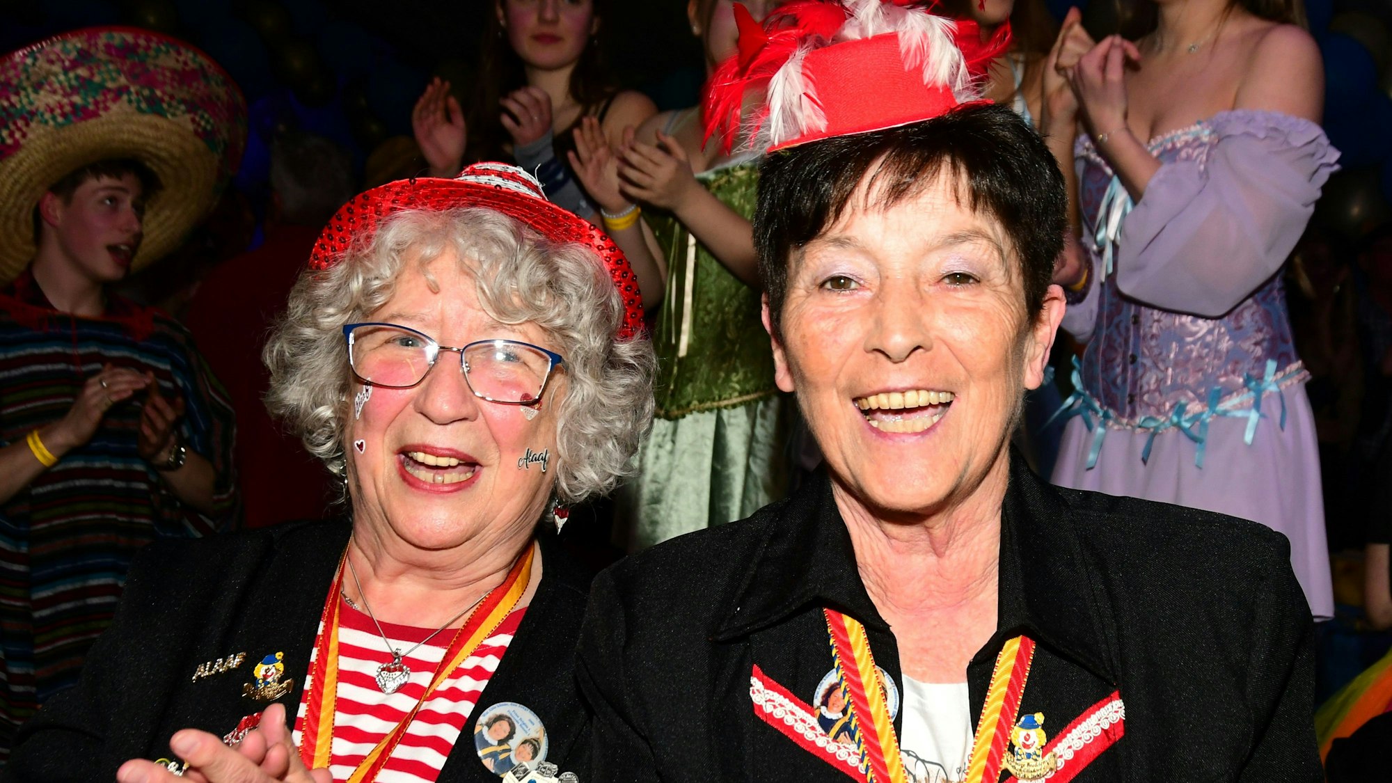 Zwei kostümierte Damen - Renate Kurth und Brigitte August - singen und klatschen auf der Karnevalssitzung mit.