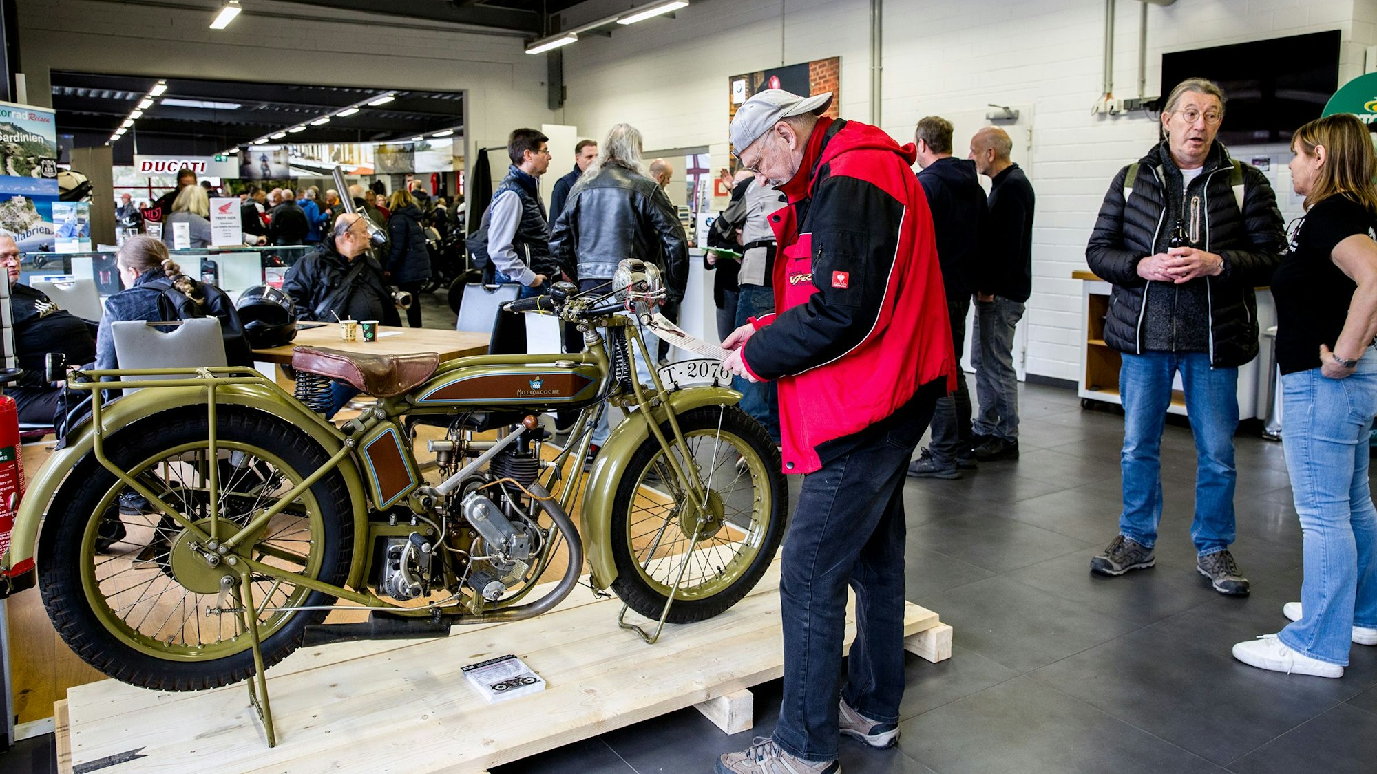 In einem Verkaufsraum stehen Motorräder und viele Kunden in Grüppchen.