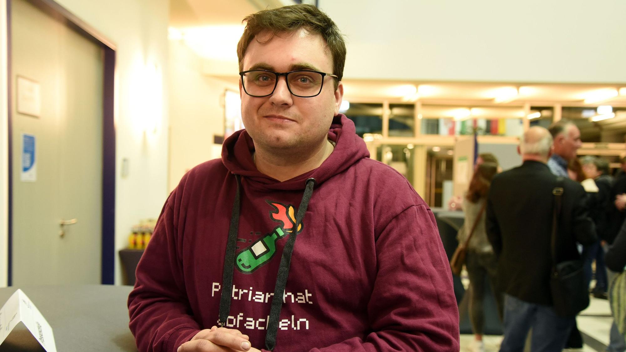 Zu sehen ist ein junger Politiker, der an einem Stehtisch steht.