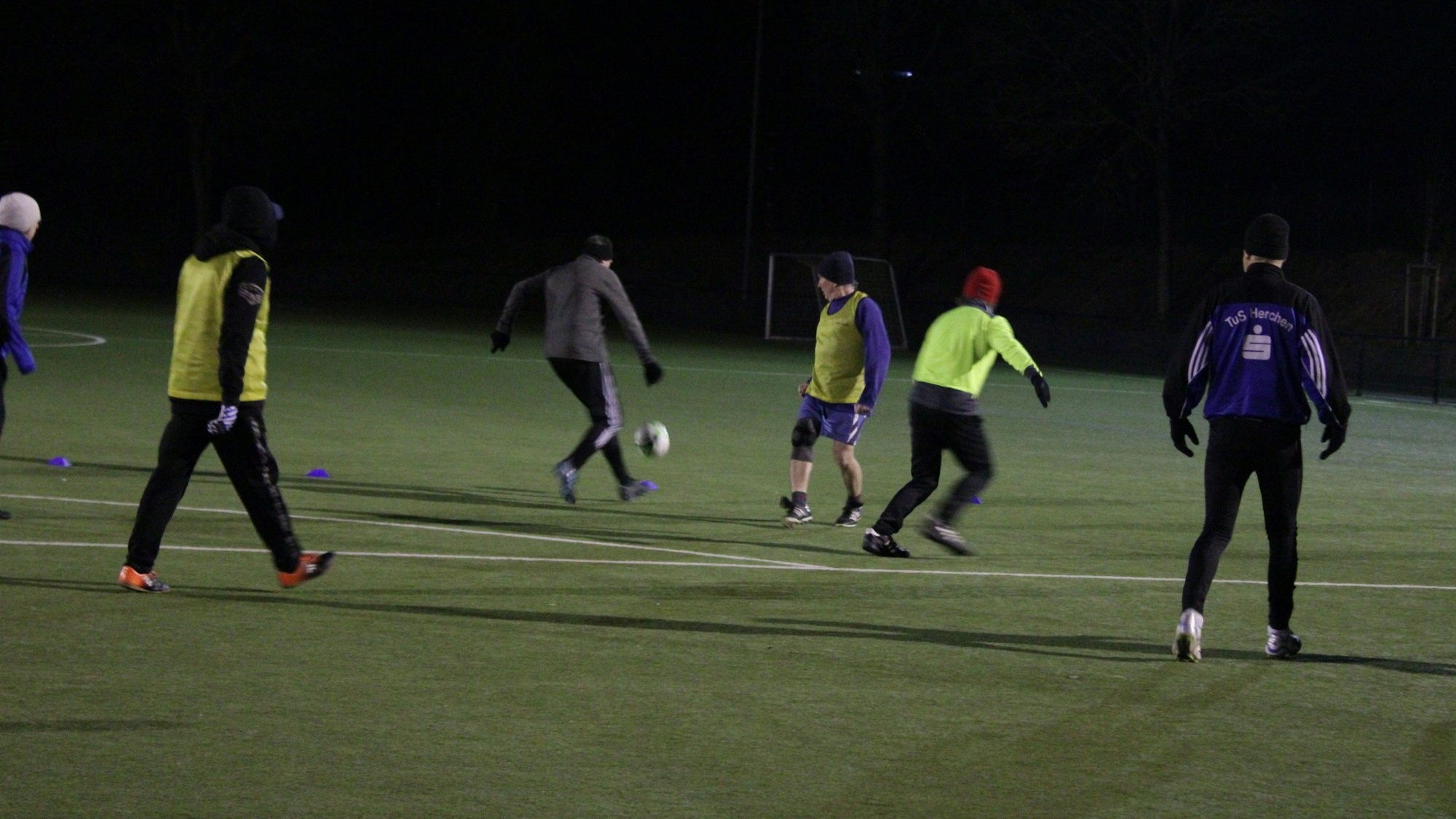 Sechs Spieler bewegen sich auf einem Fußballfeld in der Dunkelheit.